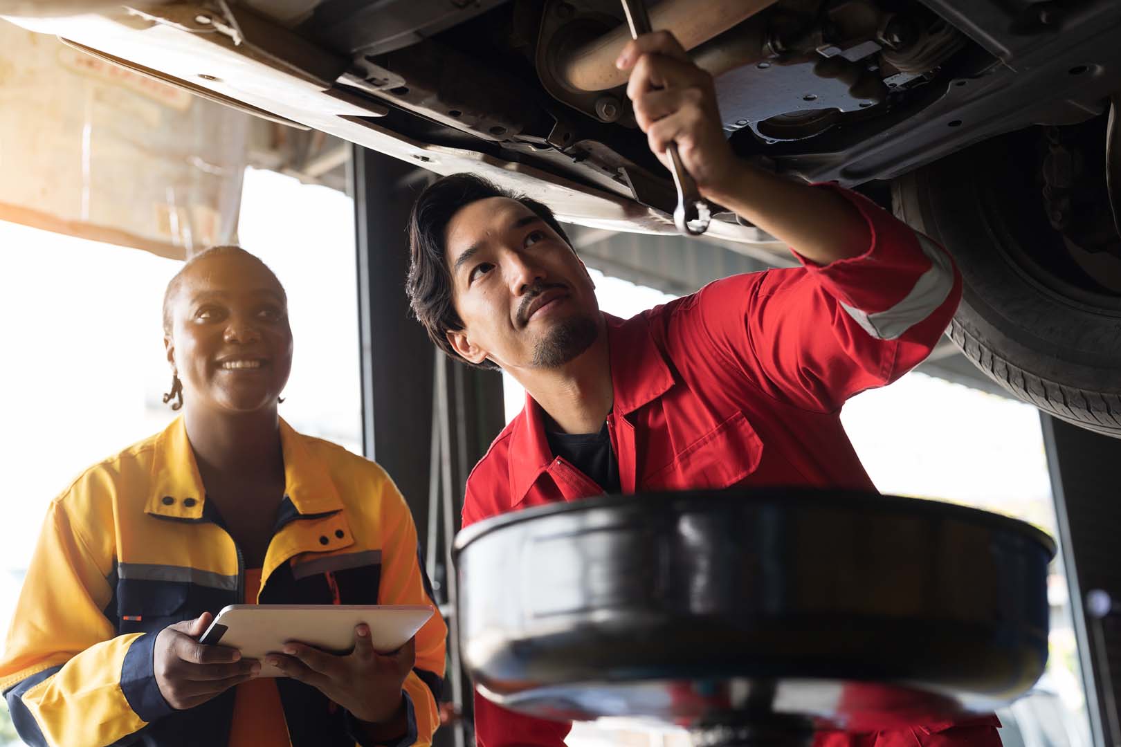 Professional mechanics check, repair and maintenance underneath lifted car at auto car repair service.