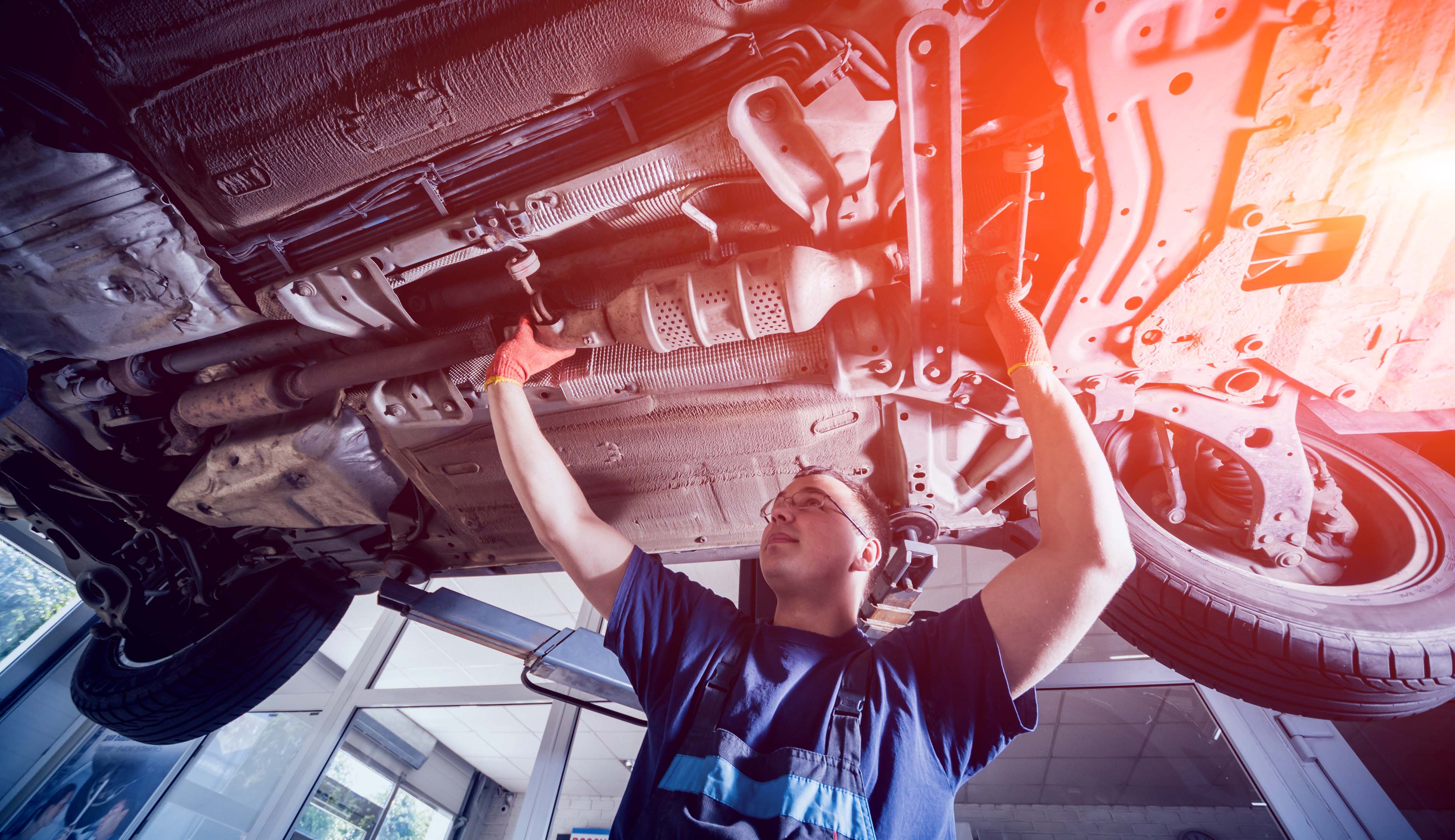 A smiling mechanic working on the underside of a car 