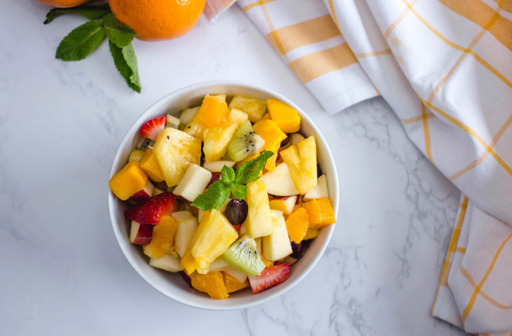 a bowl of mixed fruit salad with a sprig of mint as garnish