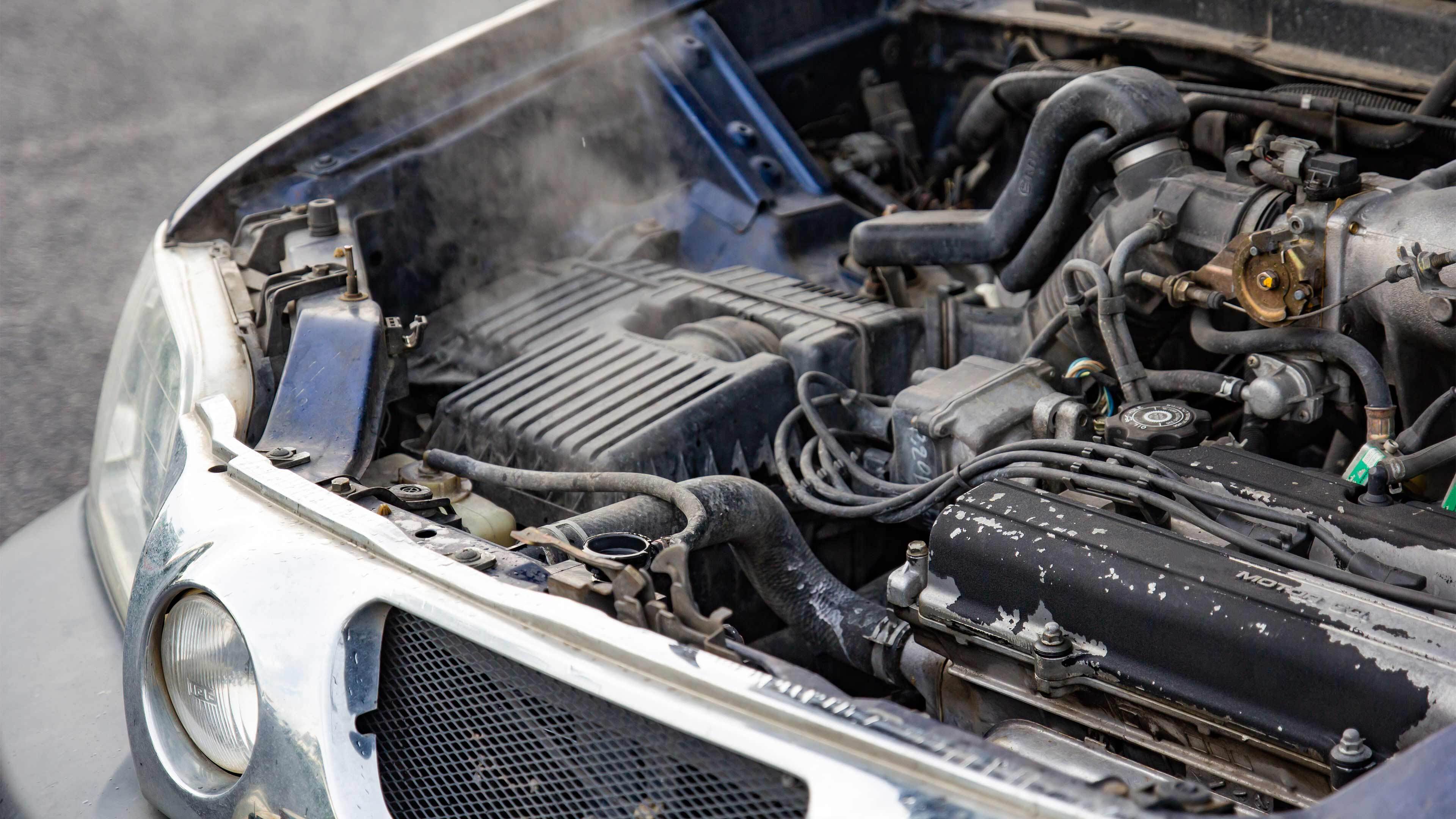 A car with its bonnet open showing the engine with smoke coming from the engine area