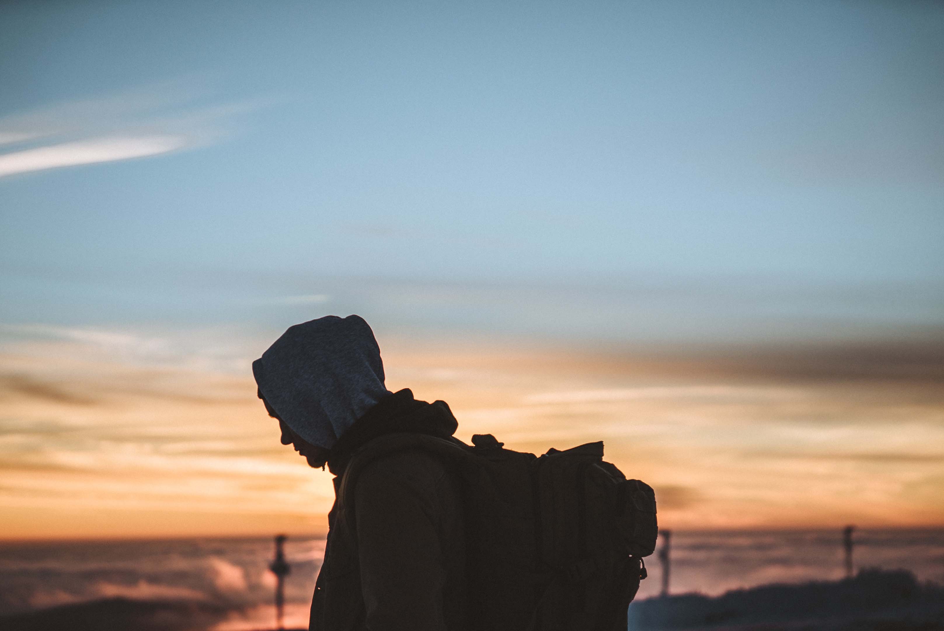 A homeless person with their hood up and rucksack on walking at dusk