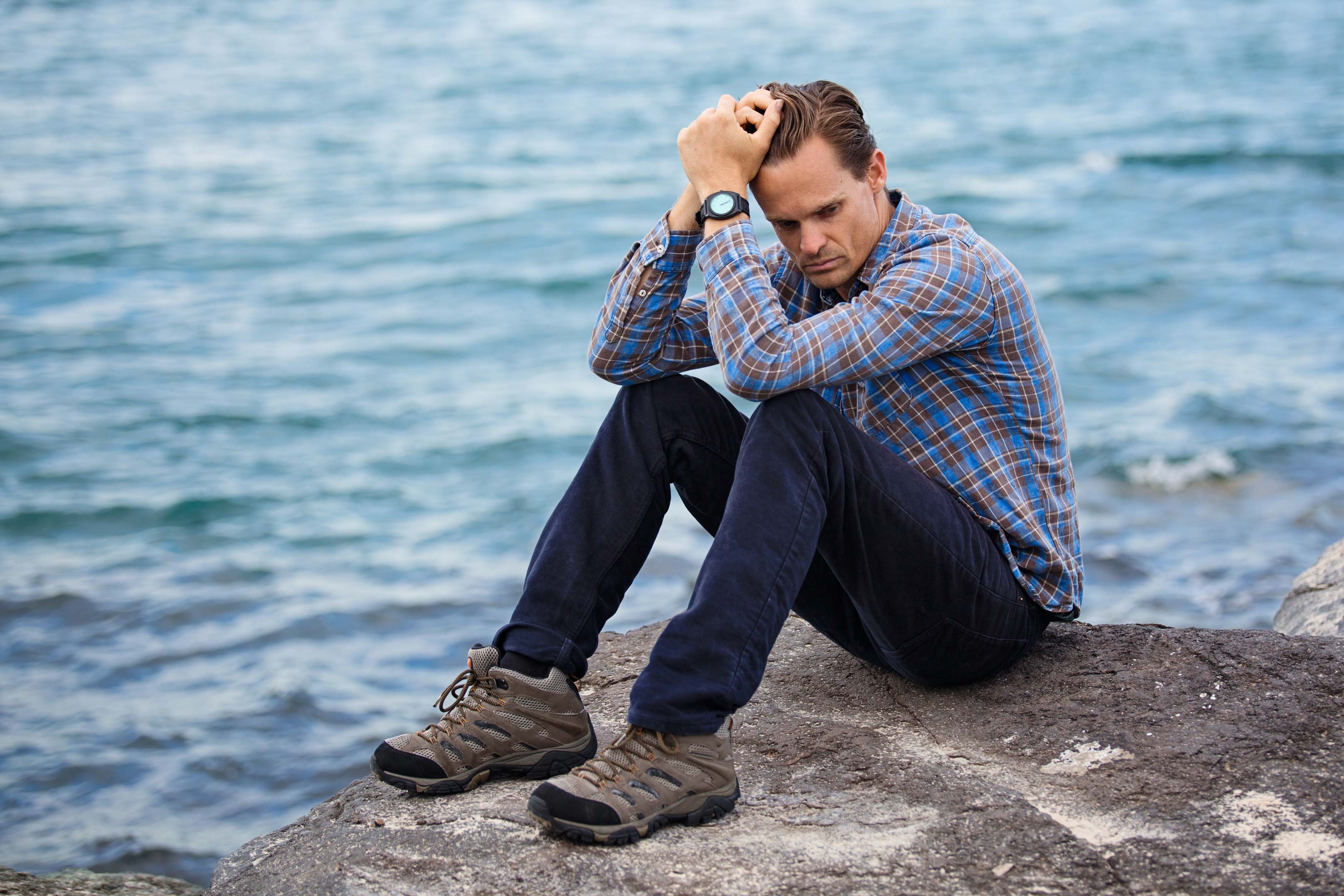 A person sitting next to the sea thinking and looking worried.