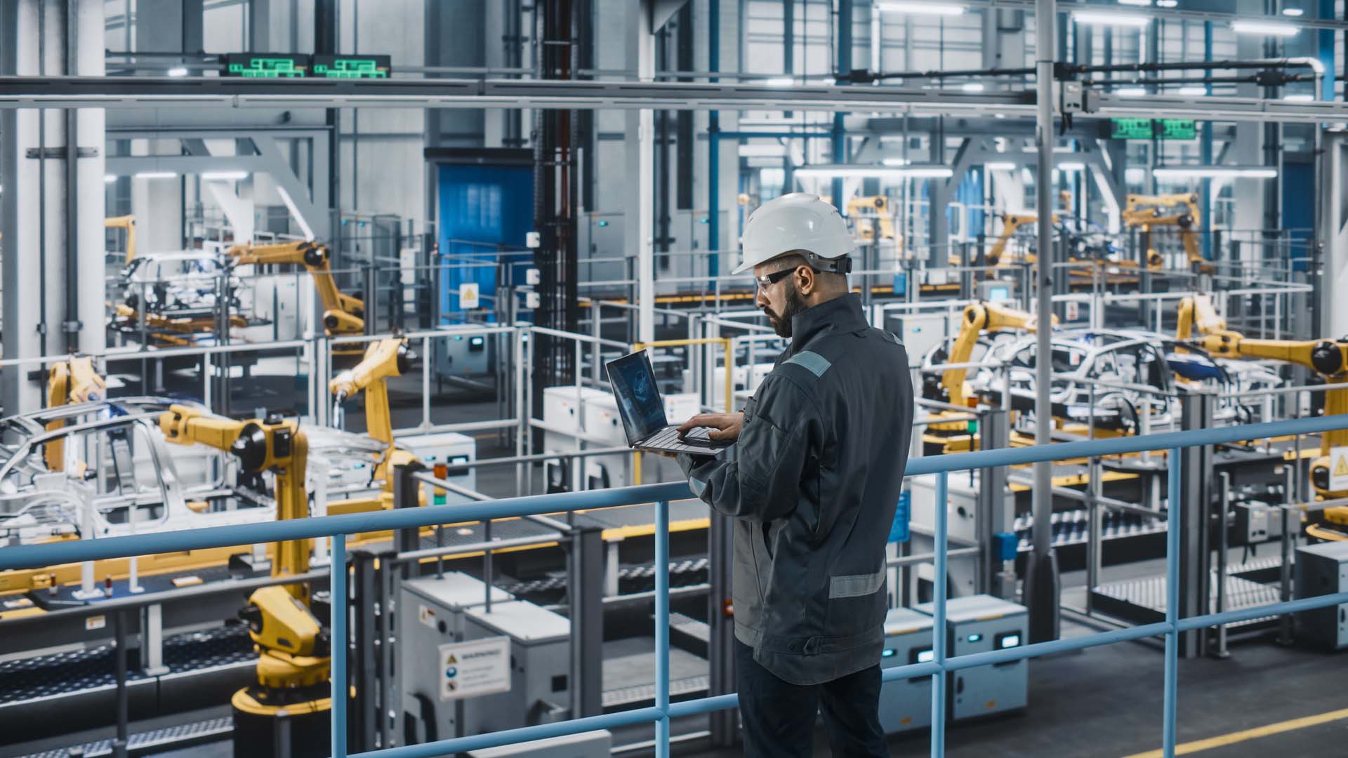 Car factory engineer working on laptop computer in an automotive industrial manufacturing facility