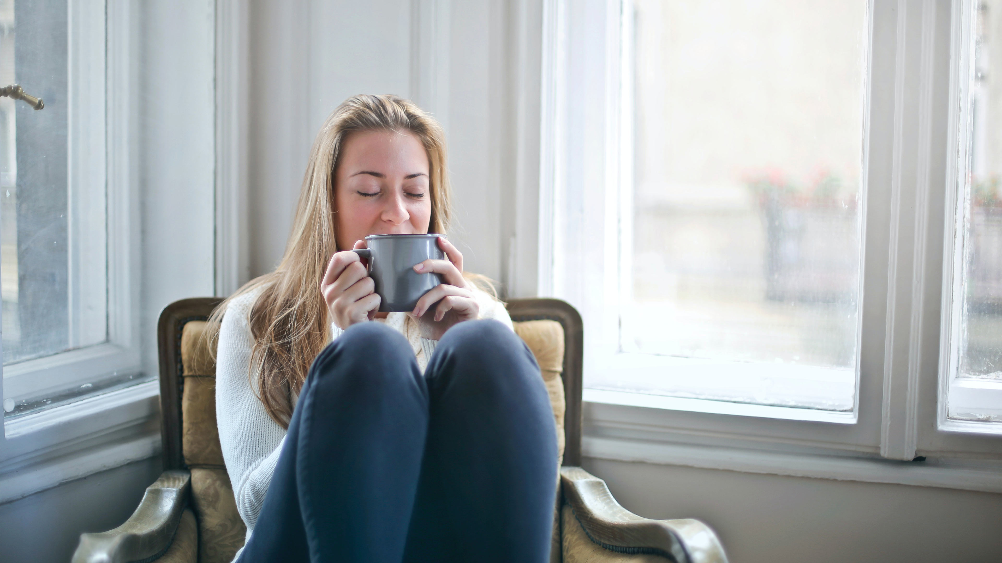 A person enjoying a hot drink with their legs curled up on chair on a wet afternoon. 
