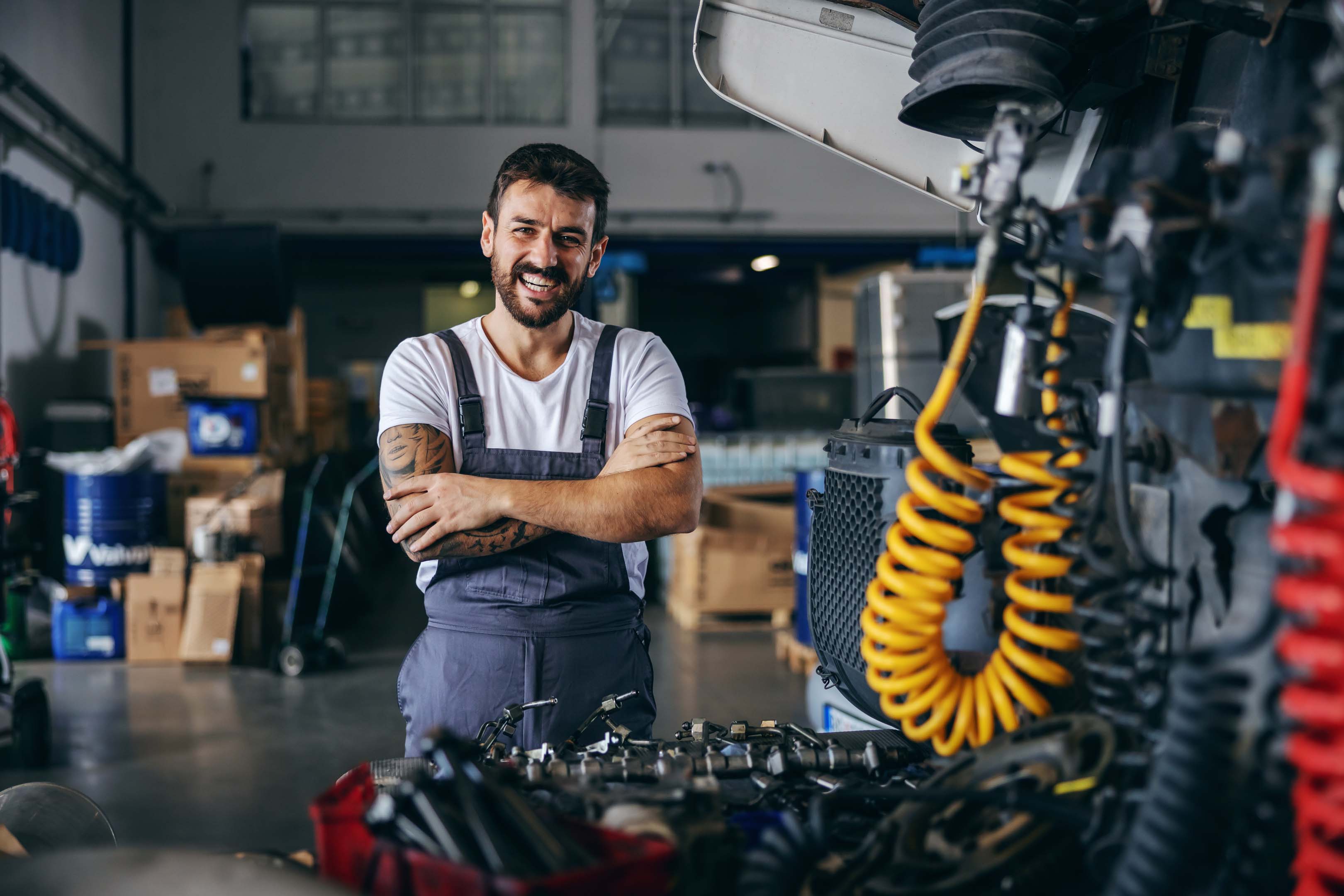 A smiling mechanic (vehicle technician) standing in a garage next to a truck being repaired