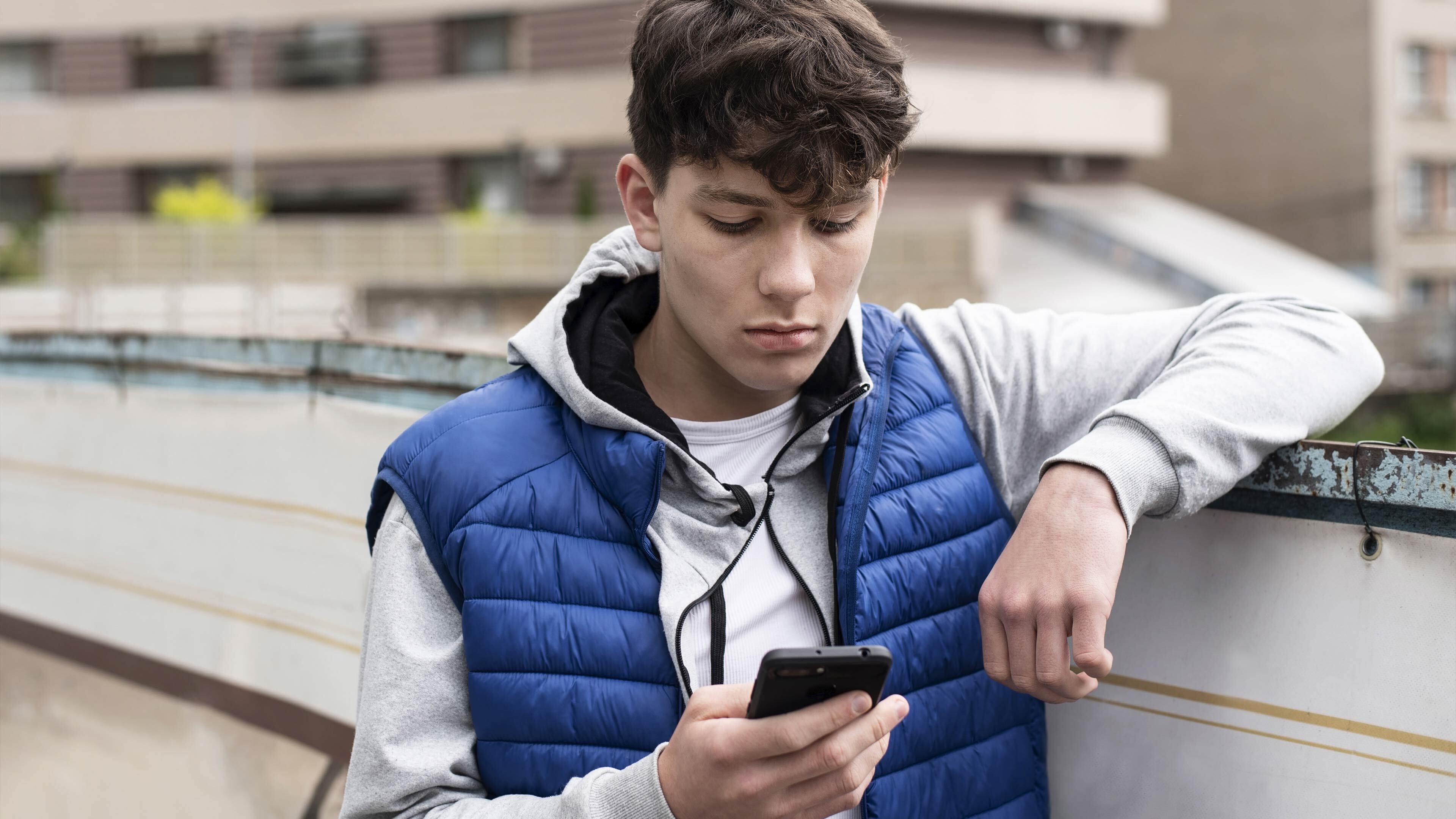 A person looking at their smart phone concerned, while leaning on a wall