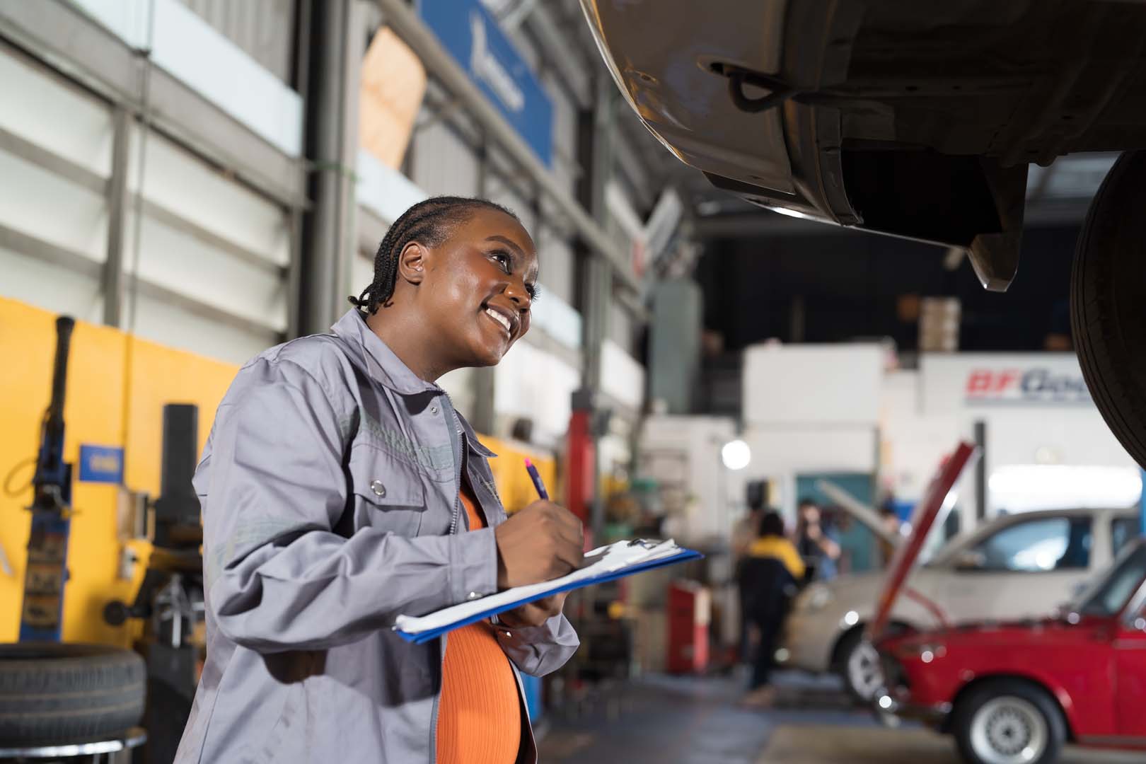Female mechanic checking car engine underneath a car on a lift at auto car repair service. 