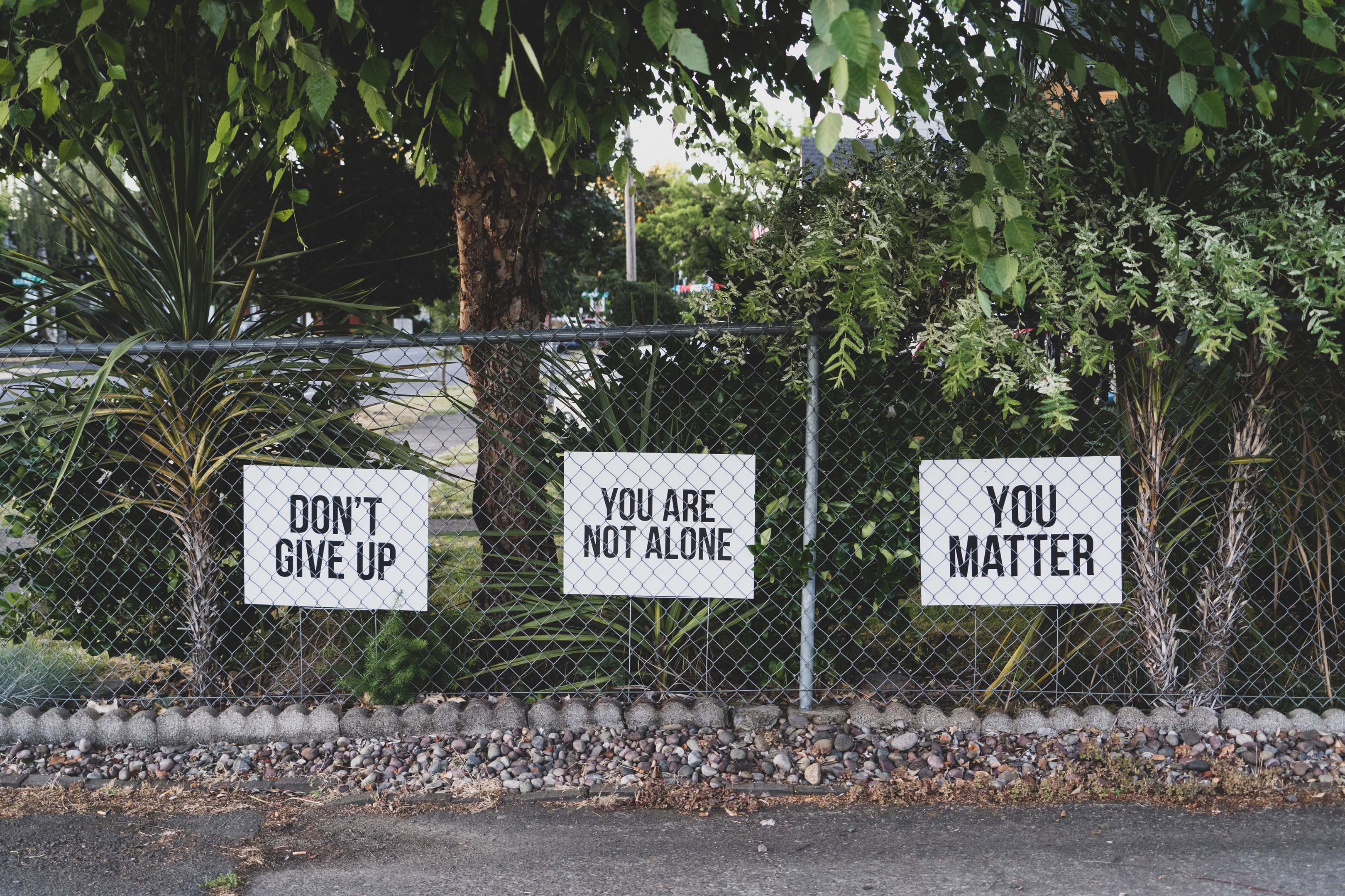 Three white signs, saying,' don't give up', 'you are not alone' and 'you matter', attached to a metal fence