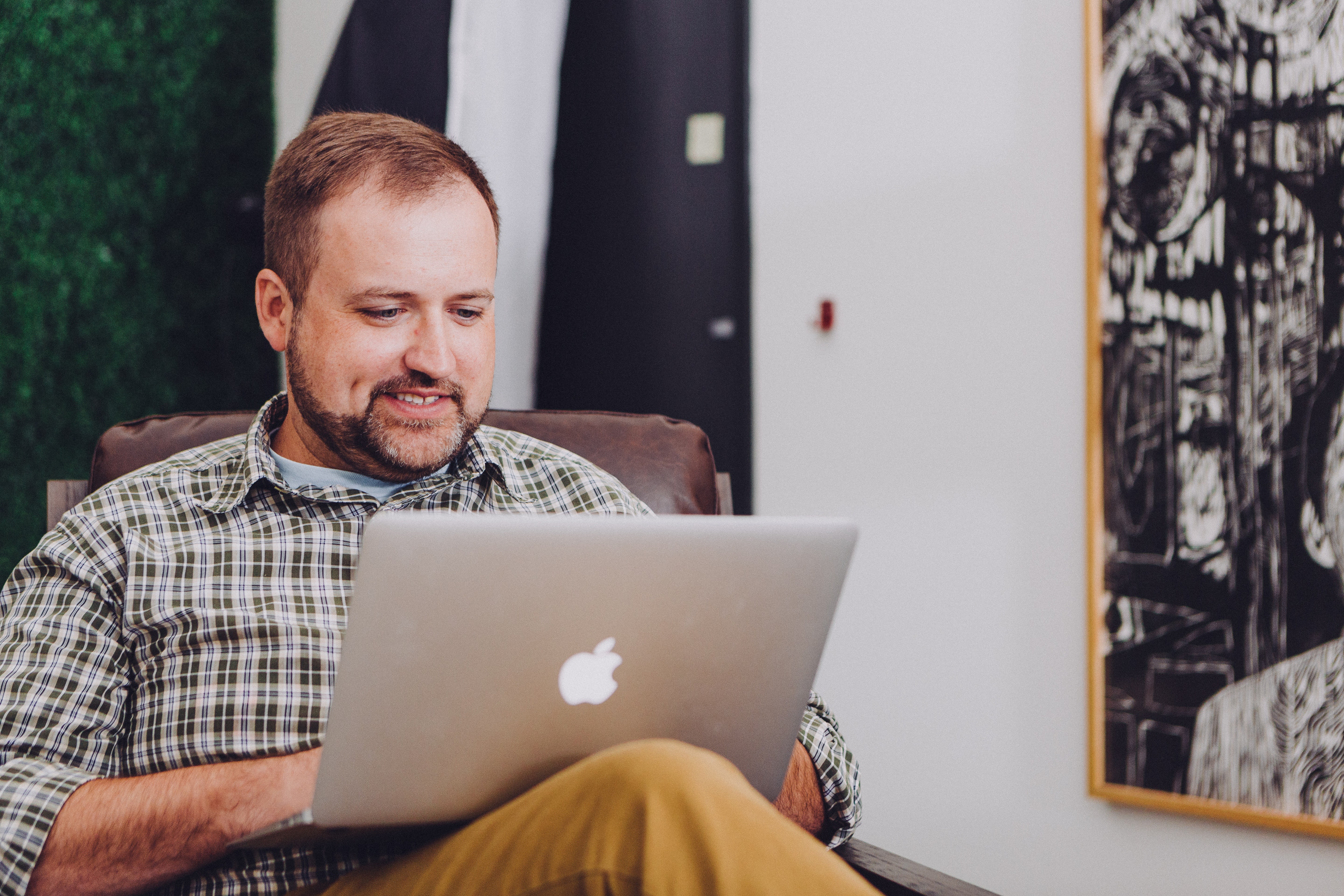 Man sitting comfortably in an armchair with his laptop, smiling