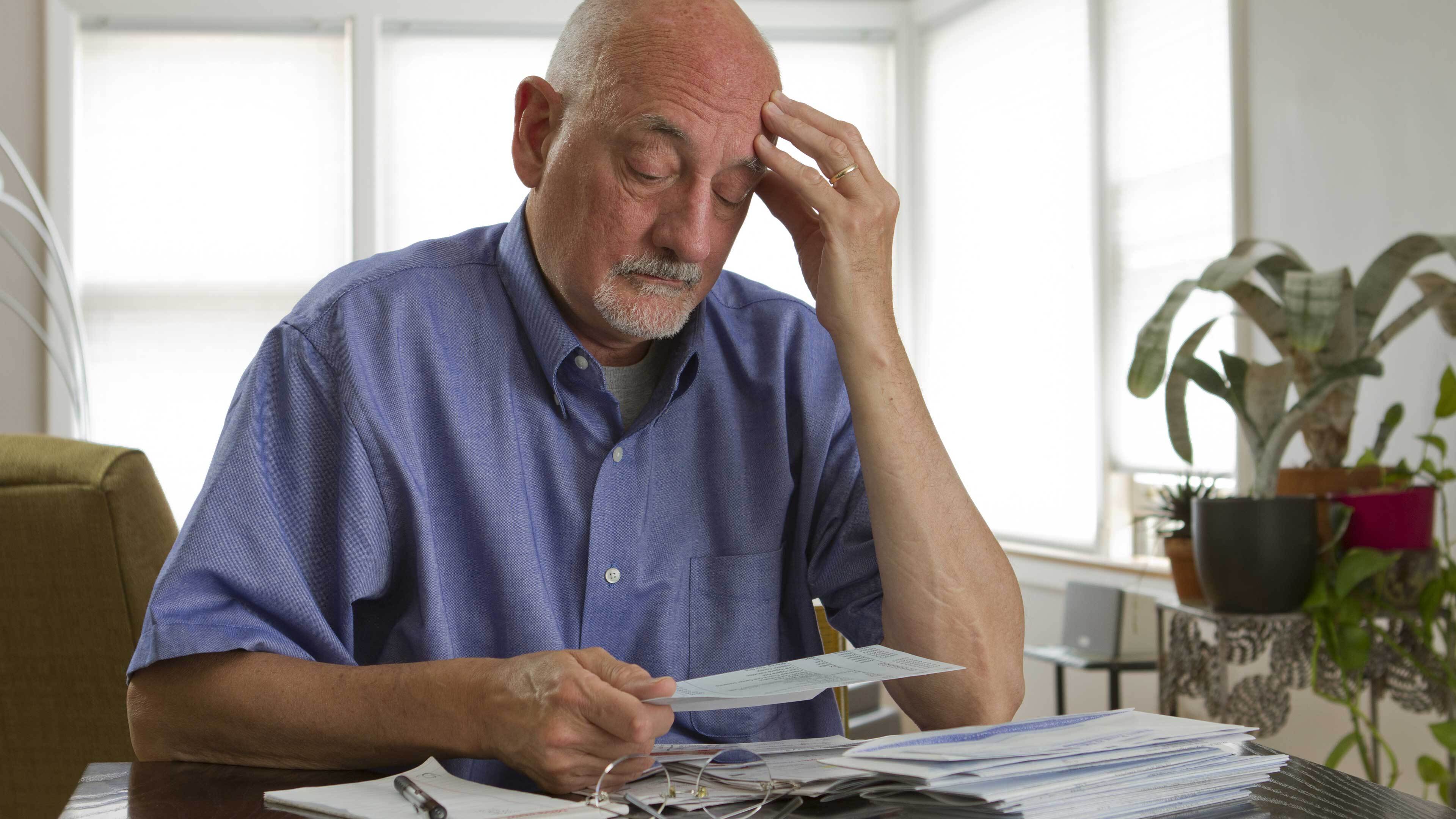 Person sat at a table with head in hands surrounded by bills looking worried about money
