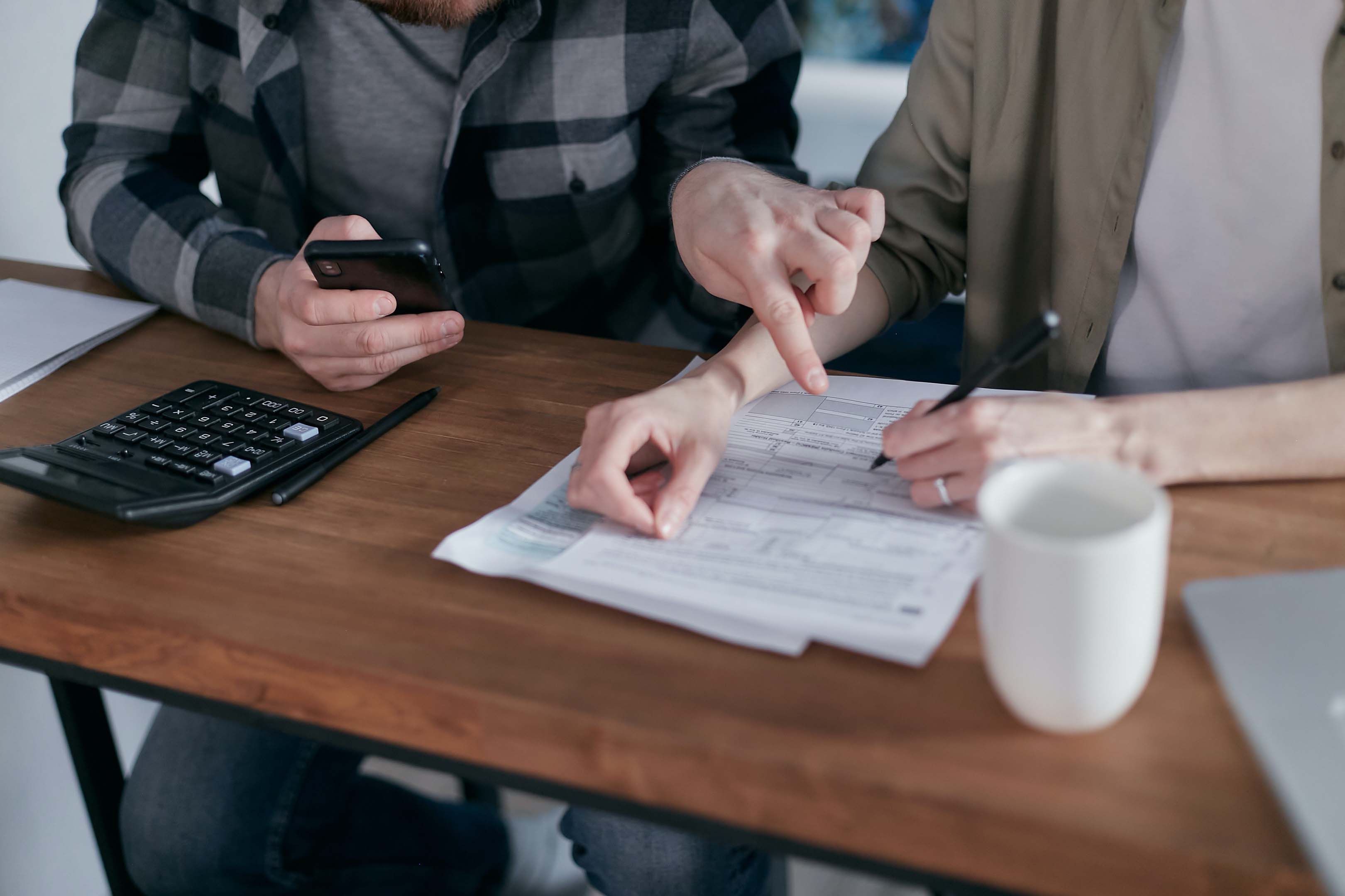 Two people sitting at a table planning using pen and paper, a smart phone and calculator