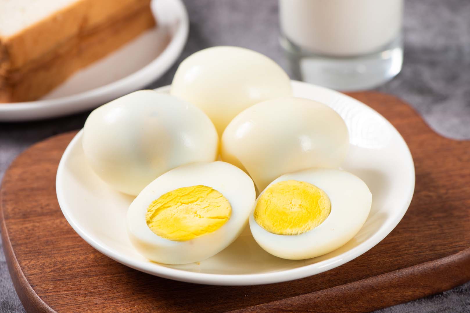 Four whole hard boiled eggs in a shallow bowl. The front egg is sliced in half.