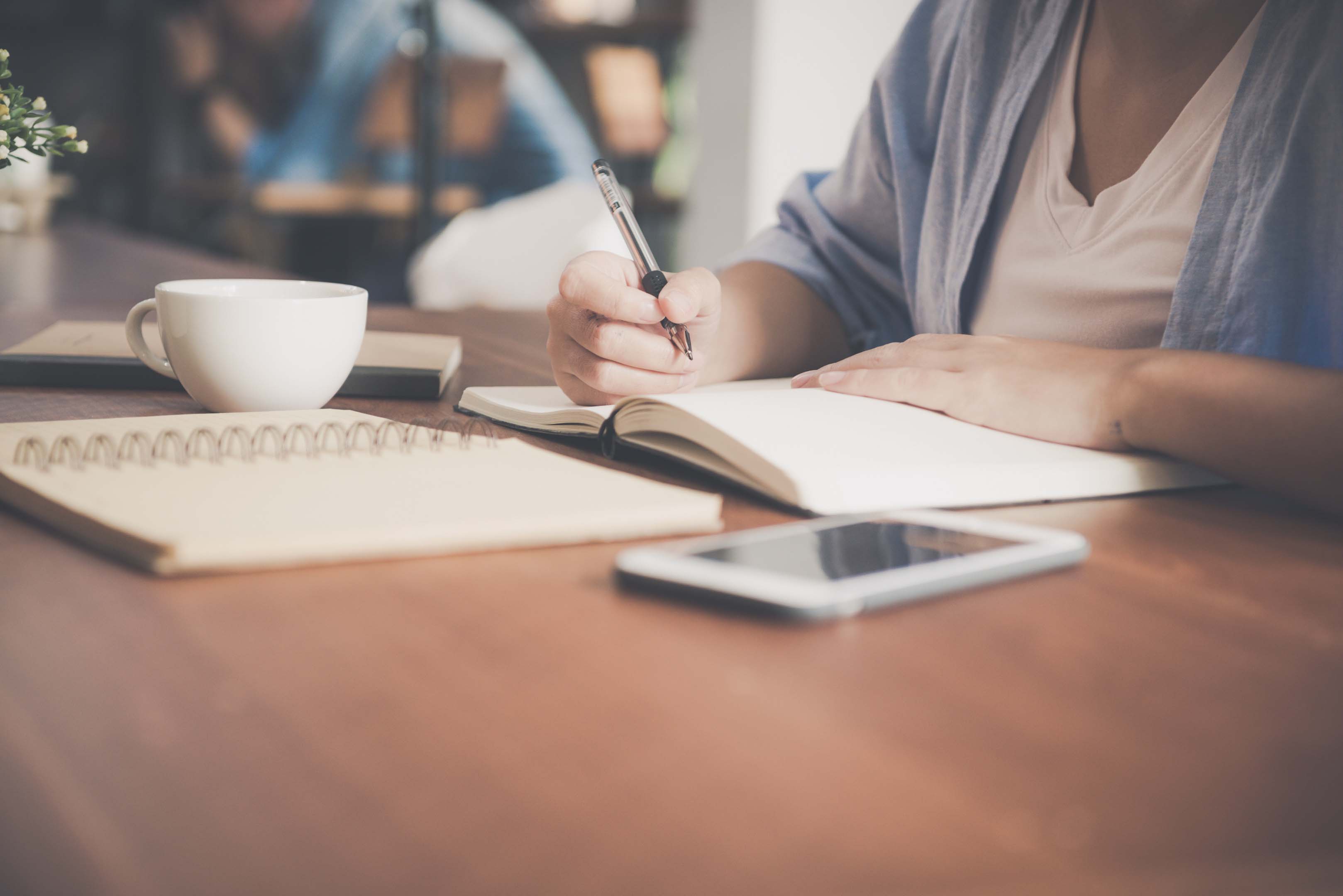 Person sitting with a hot drink, writing down notes in preparation for a job interview