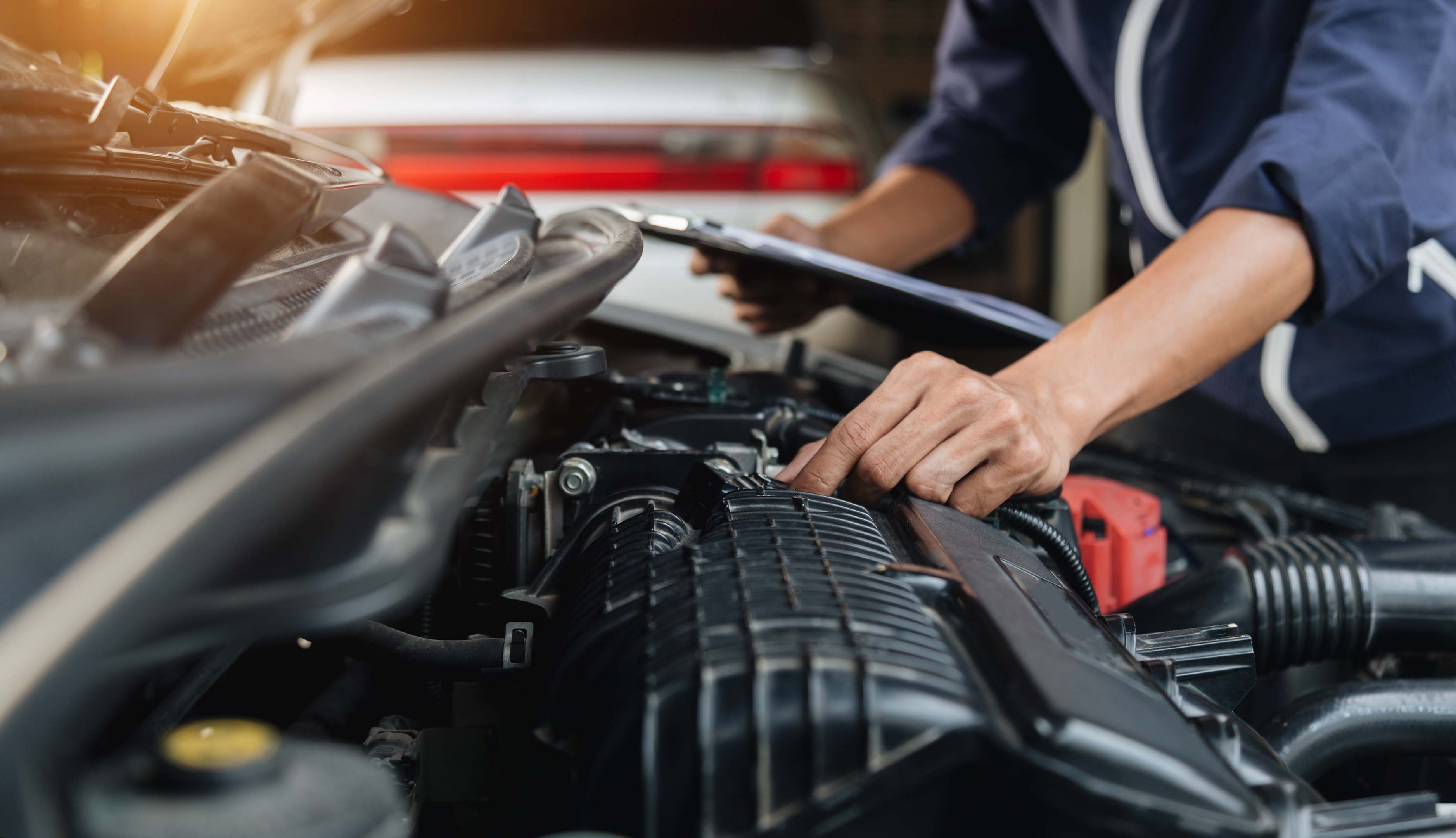 Vehicle technician (mechanic) examining a car engine in an automotive workshop (garage)