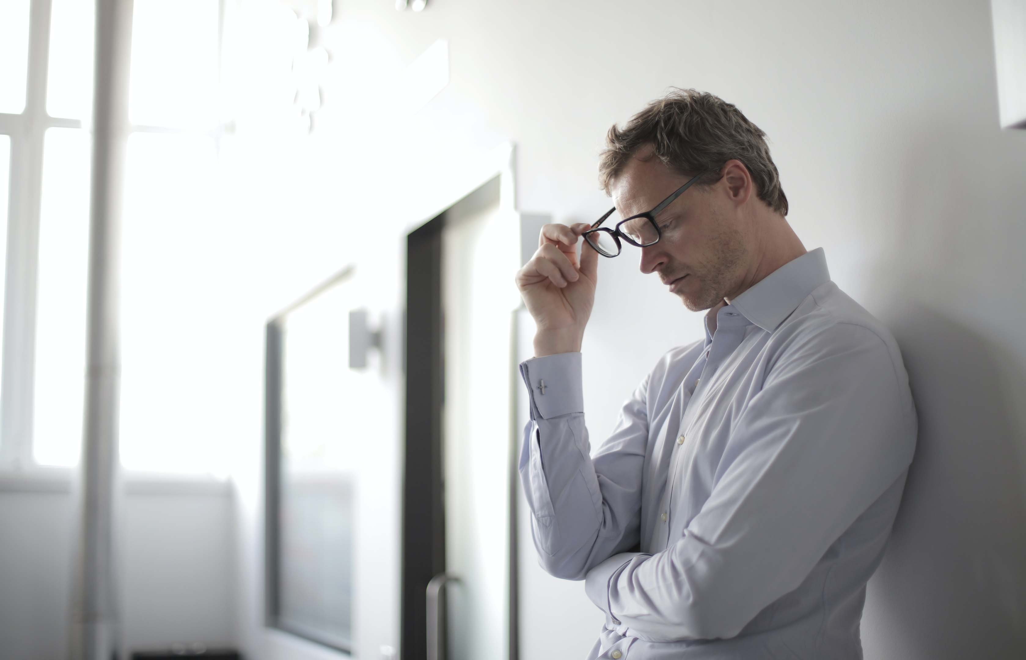 Person wearing a shirt leaning against a wall looking down to the ground with a worried expression 
