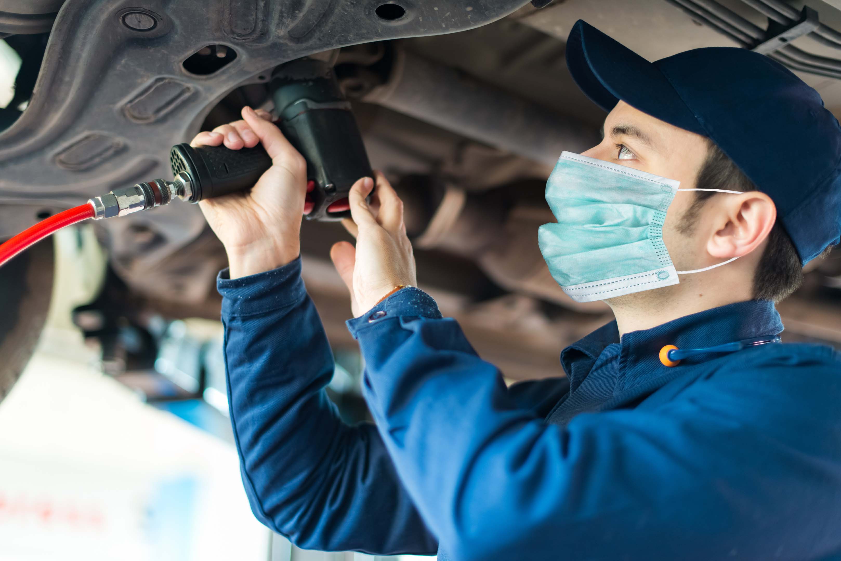 Mechanic wearing a face mask working on the underside of a car
