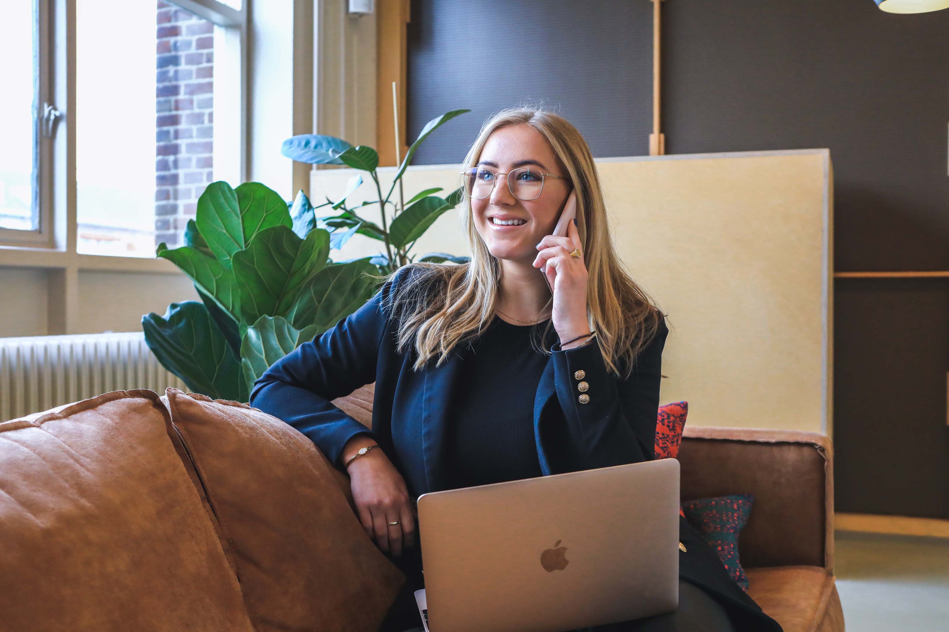 Woman in smart clothing, sitting with laptop, smiling while having a telephone interview