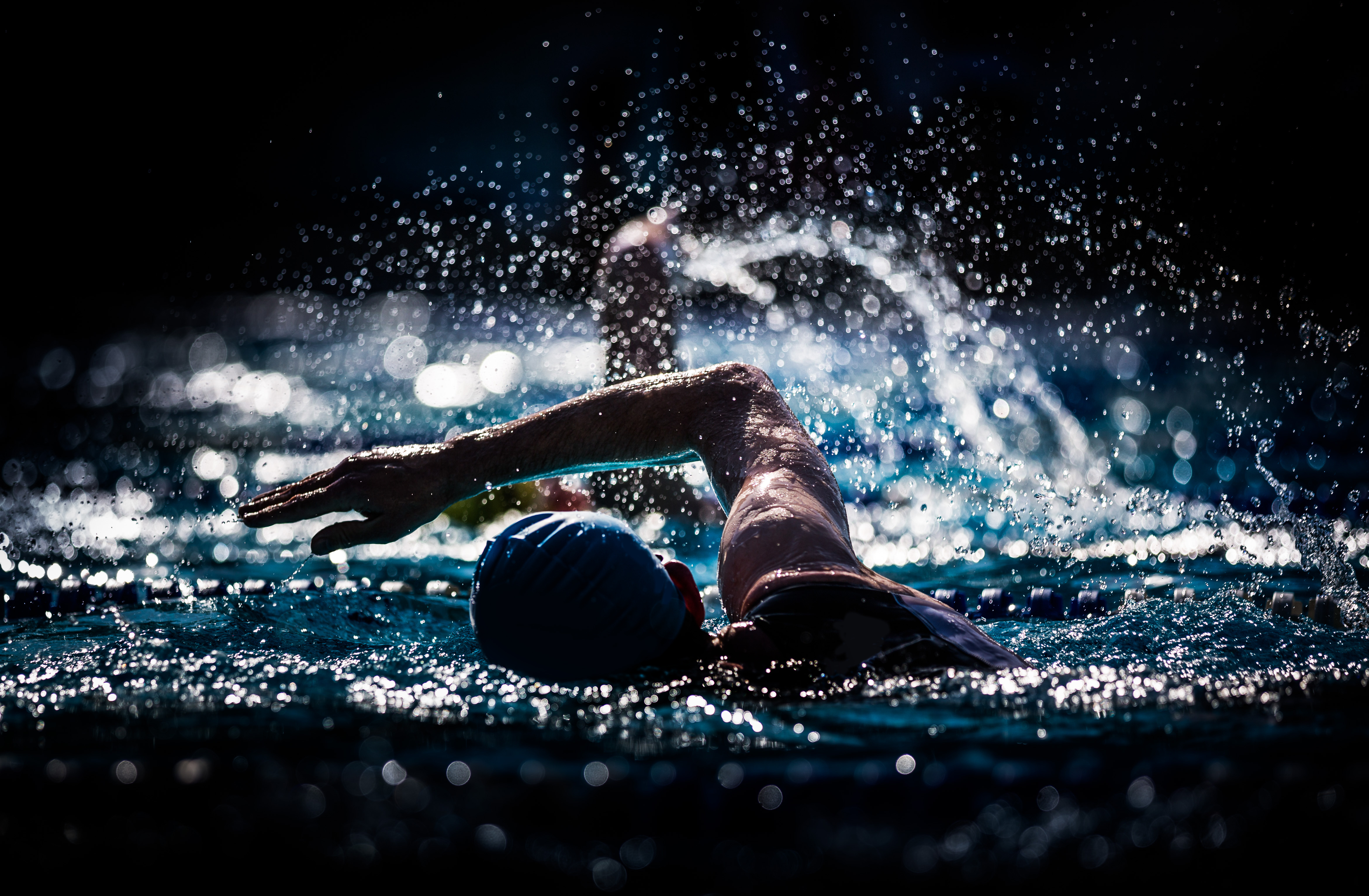 Swimmers, swimming through lanes wearing swimming caps  